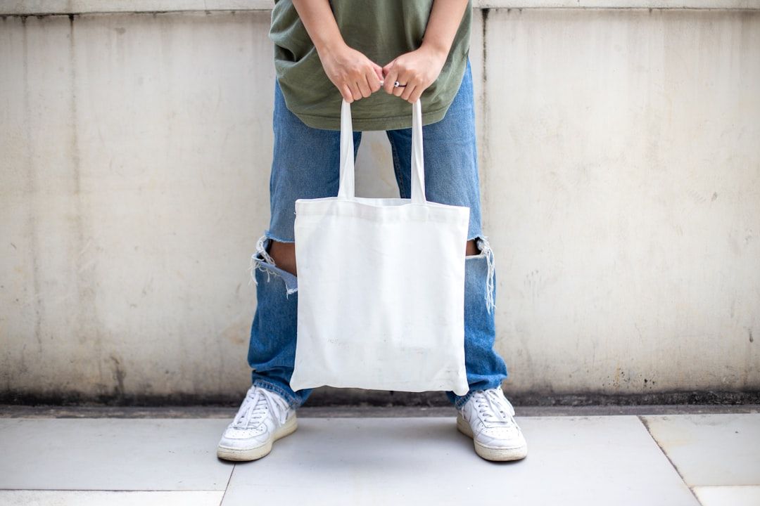 En person i trasiga jeans håller i en tom, vit tygpåse.