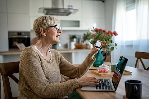 En äldre kvinna använder sin bärbara dator och håller i ett betalkort.