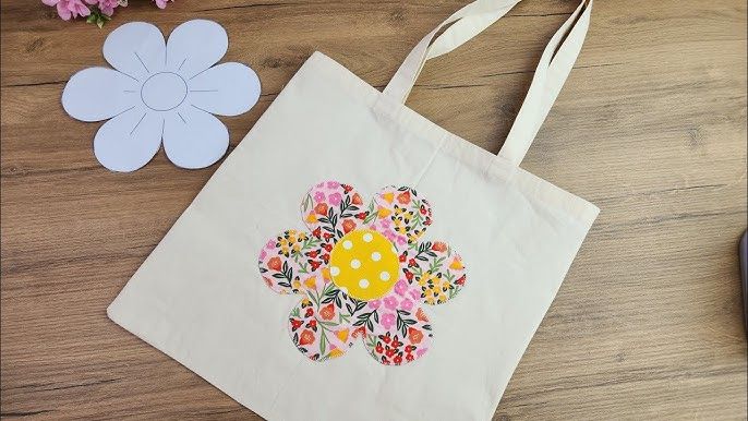 En beige tygpåse med ett blommigt applikationsmotiv på ett träbord.