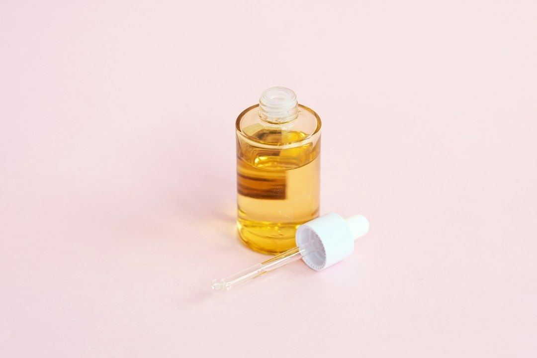Öppen glasflaska med gyllene serum och pipett på rosa bakgrund